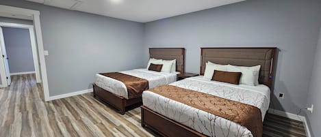 A hotel room with two beds, a wooden floor, and a grey wall.