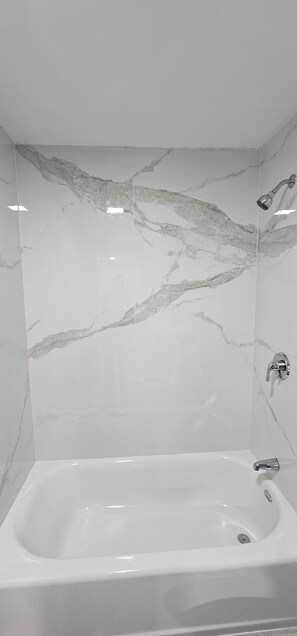 A modern bathroom with a marble wall, a bathtub, and a showerhead.