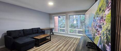 A modern living room with a sectional sofa, a wooden coffee table, and a large TV screen displaying a scenic view.