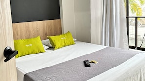 Una habitación de hotel con una cama, un edredón gris, un control remoto y una almohada verde.