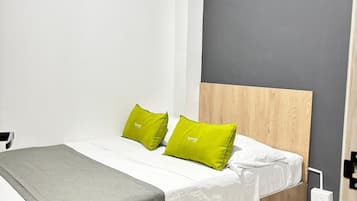 Una cama bien hecha con ropa blanca y dos almohadas verdes, una manta gris y un cabecero de madera.