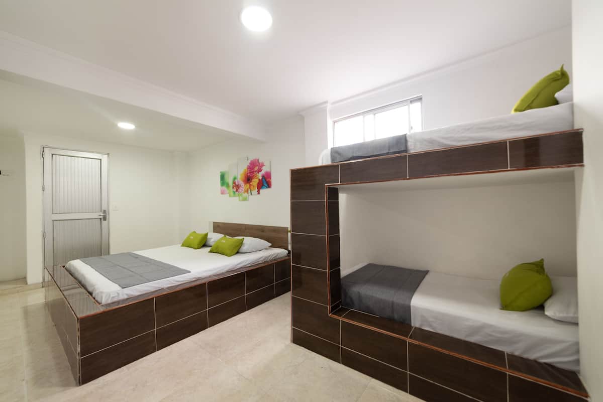 A room with two beds, one with a headboard and one with a bunk bed, both with pillows and a blanket.