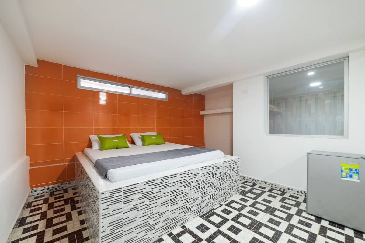 A small, modern room with a bed, a window, and a refrigerator.