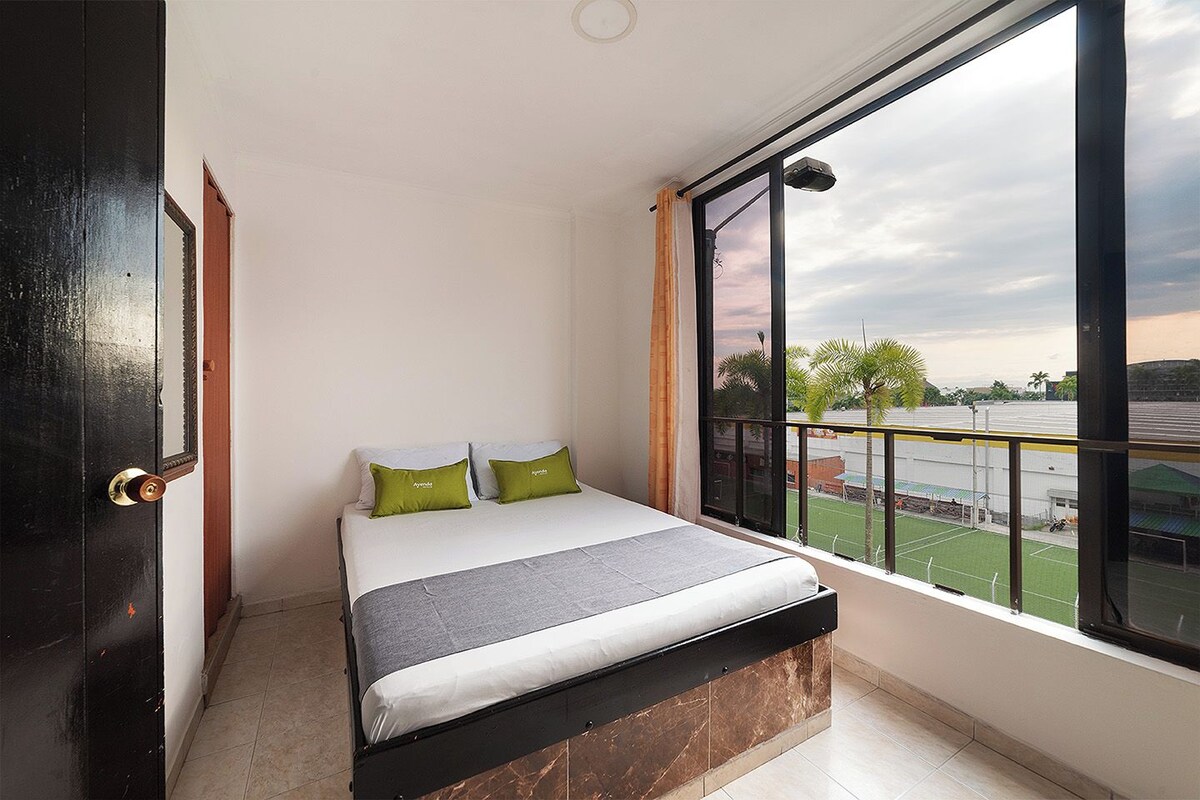 A room with a bed, a large window, and a view of a sports field.