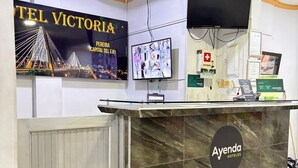 Una recepción de hotel con un cartel grande que dice 'Hotel Victoria' y una pantalla digital.