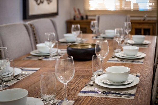 Une table à manger dressée avec de l’assiette blanche, des bols et des verres à vin, le tout posé sur une table en bois agrémentée de sets de table.