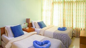 Une chambre d’hôtel avec deux lits, une table de chevet avec une lampe, une fenêtre avec des rideaux à motifs floraux et un climatiseur au plafond.