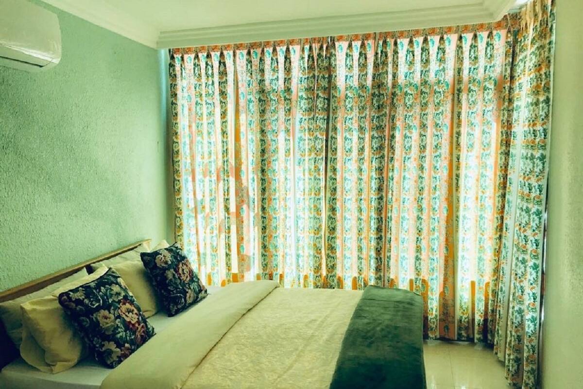 A bedroom with a bed, floral curtains, and a green wall.