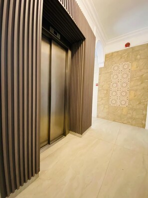 Un ascensor de diseño moderno, una pared de piedra con un panel decorativo y un suelo de baldosas.