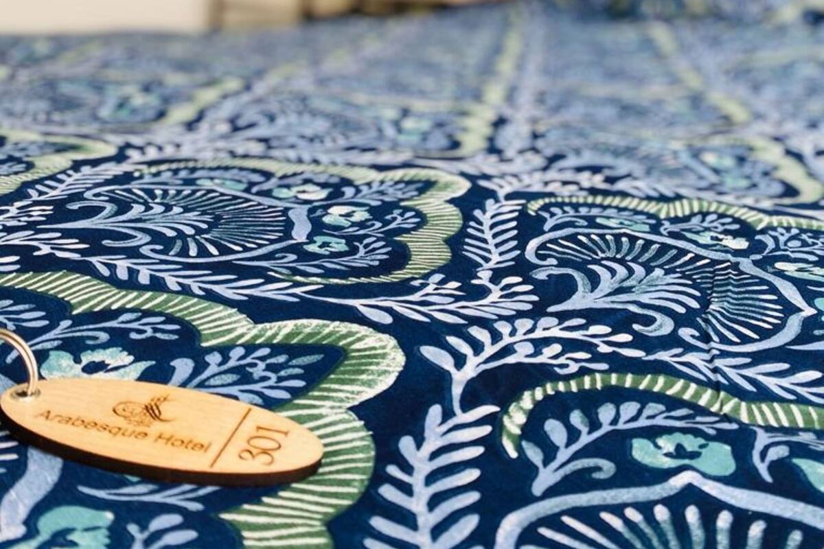 A bed with a patterned blue and green bedspread, a wooden tag with "Arabeque Hotel" and room number "301".