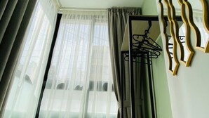 Une pièce comprenant un lit, une chaise, une fenêtre avec des rideaux légers et un porte-manteau fixé au mur.