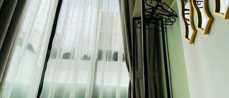 A room with a bed, a chair, a window with sheer curtains, and a wall-mounted coat rack.