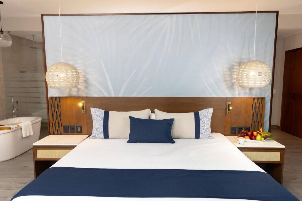 Een moderne hotelkamer met een groot bed, twee nachtkastjes, een badkuip en een fruitschaal.