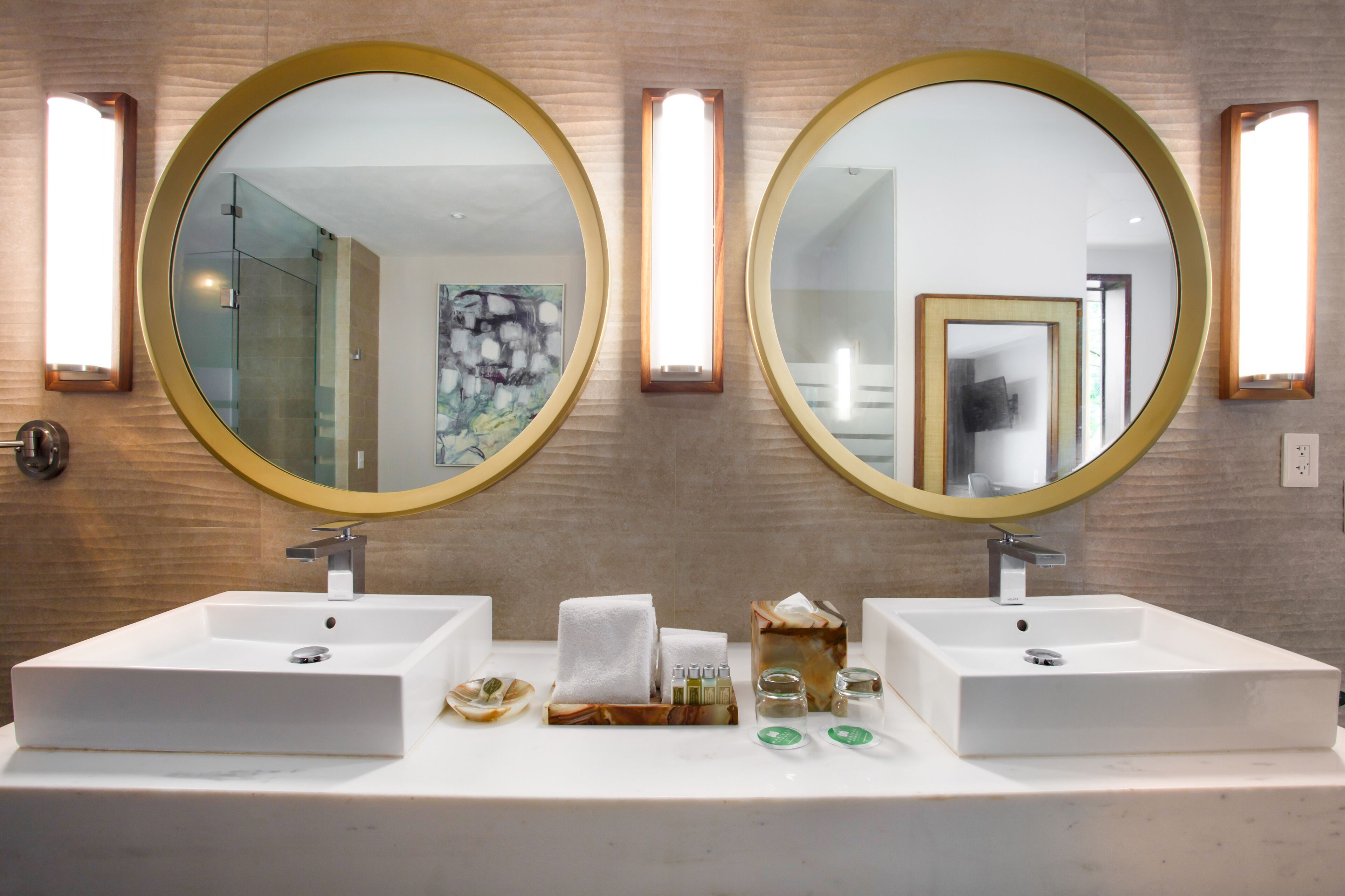 A bathroom with two sinks, each with a round mirror and a light above. There are toiletries on the counter.