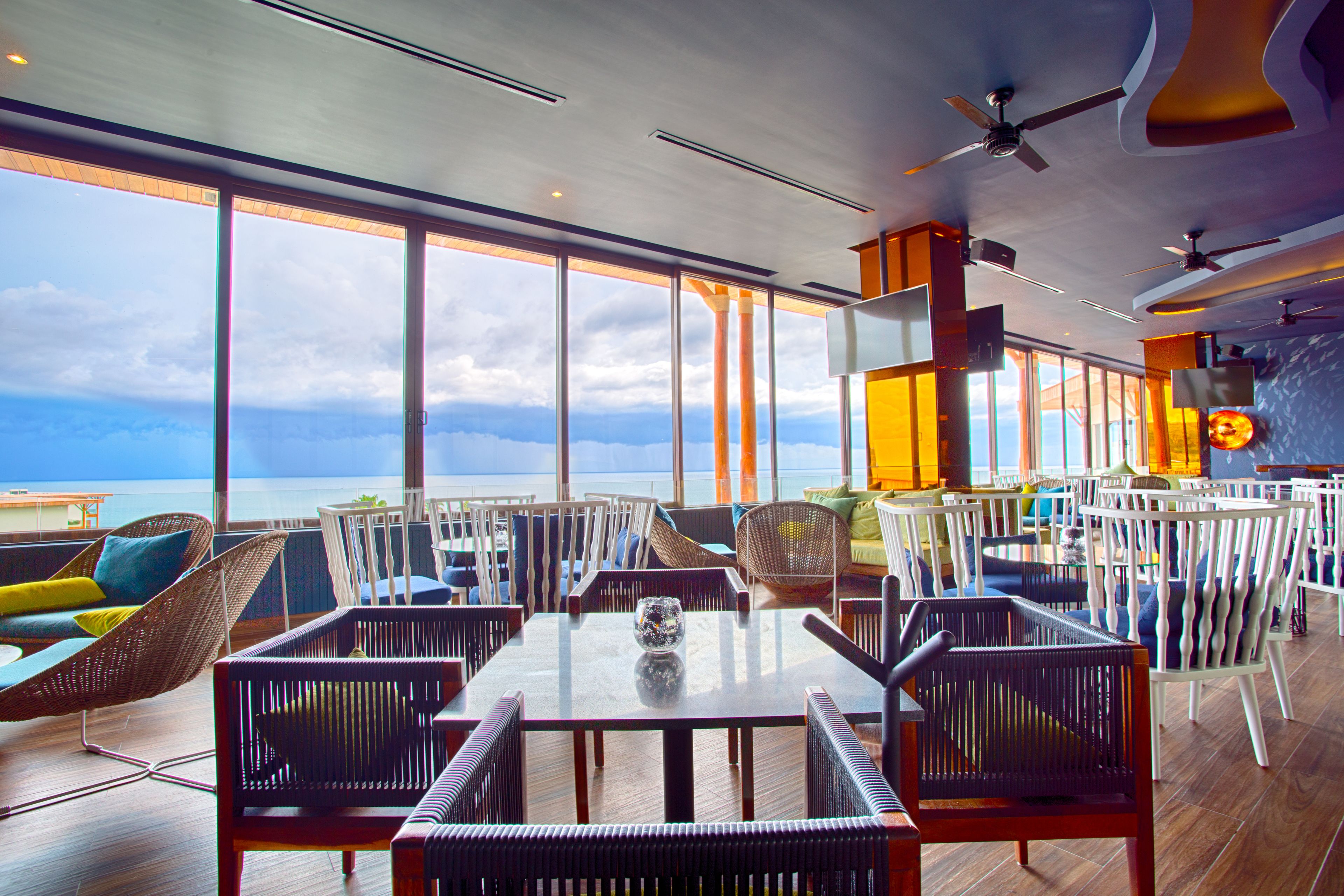 A spacious indoor area with large windows offering a view of the ocean. There are multiple seating arrangements including wicker chairs and tables.