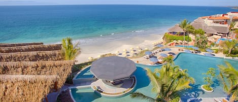 Un resort con una amplia piscina, playa y construcciones de techo de paja.