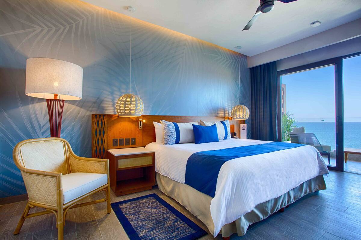 Een moderne hotelkamer met een groot bed, een stoel, een nachtkastje en uitzicht op zee.