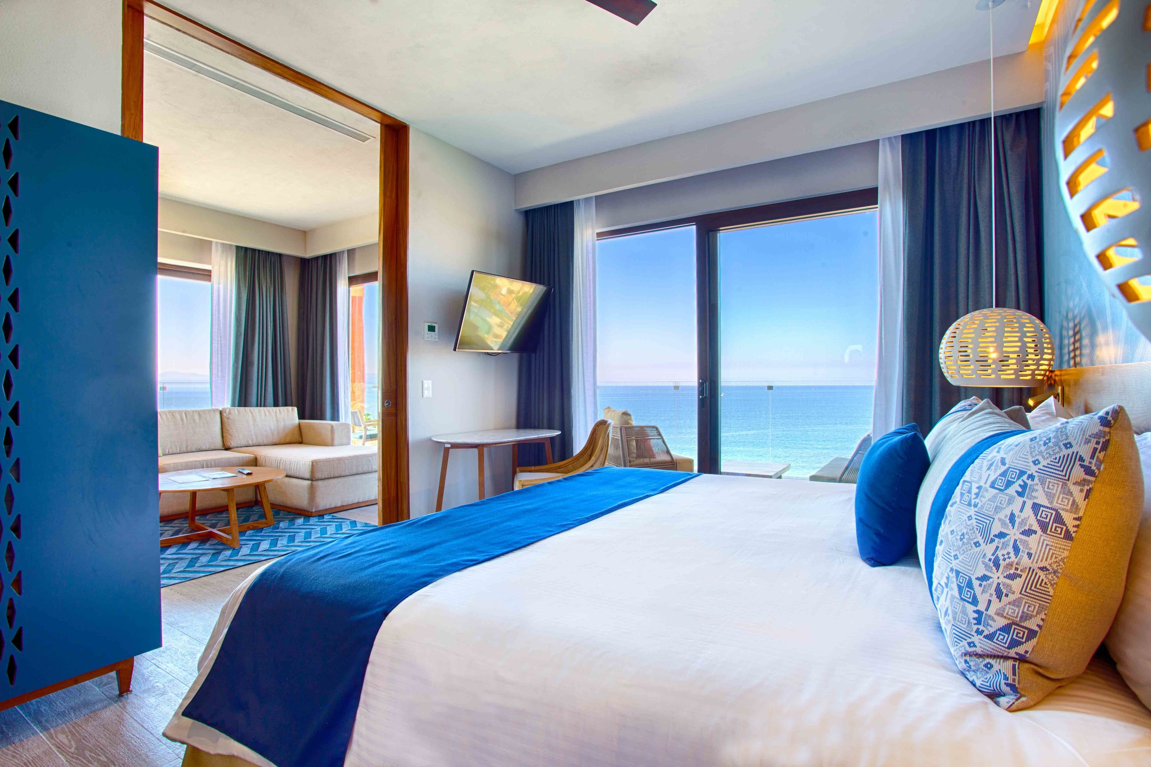 A hotel room with a large bed, a sofa, a small table, and a view of the ocean.