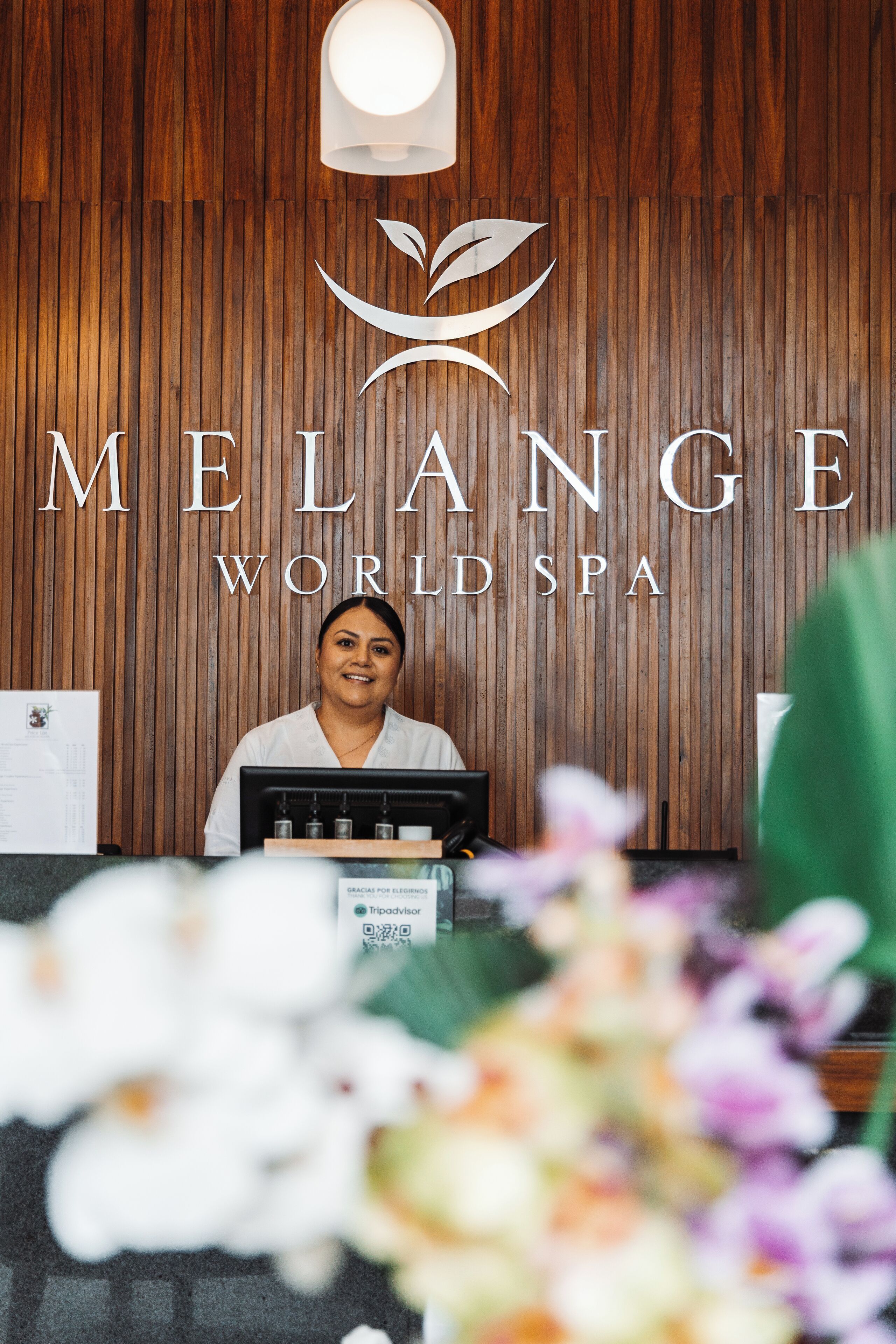 A reception desk at Melange World Spa with a wooden backdrop and a logo above.