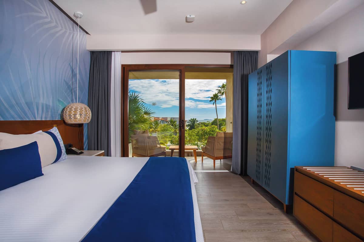 Een hotelkamer met een groot bed, een bureau, een stoel, een kledingkast en uitzicht op het omliggende landschap.