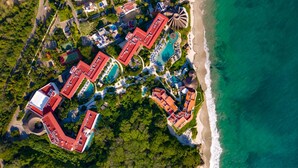 Vue aérienne d’un complexe hôtelier comprenant plusieurs bâtiments, une plage et une grande étendue d’eau.