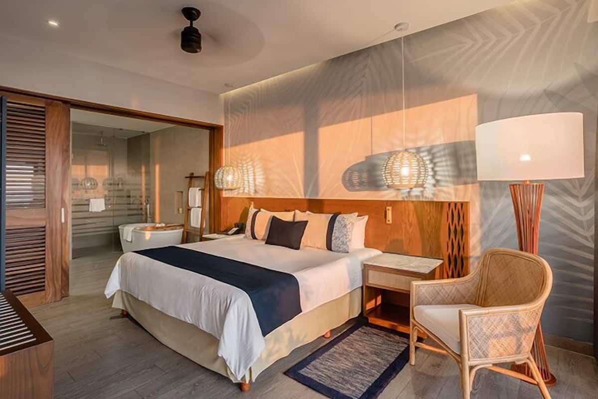 Een moderne hotelkamer met een groot bed, een zithoek met een stoel, een bureau en een groot raam.