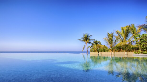Une piscine à débordement à l’eau d’un bleu cristallin, bordée de palmiers et offrant une vue sur l’océan.