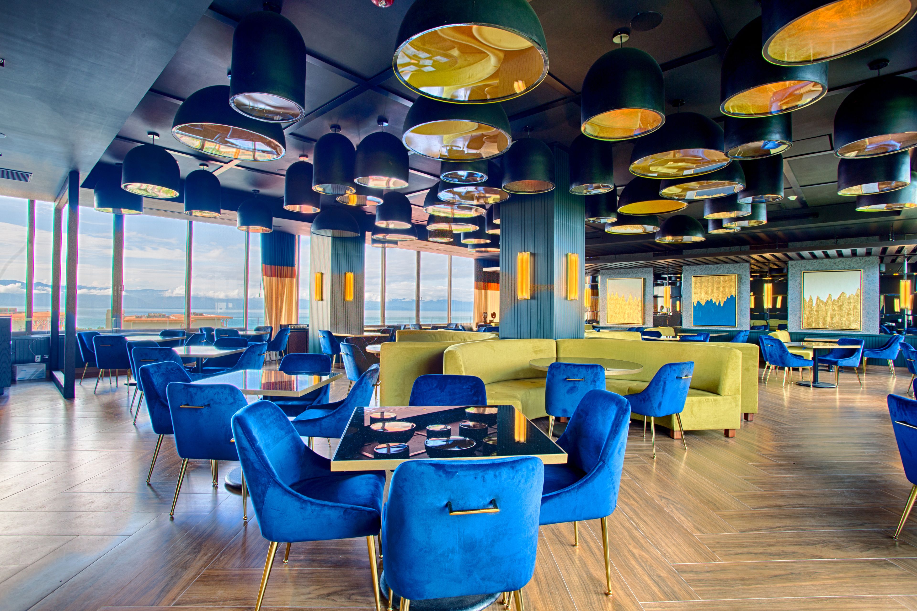 A modern restaurant with blue and yellow seating, large windows, and hanging pendant lights.