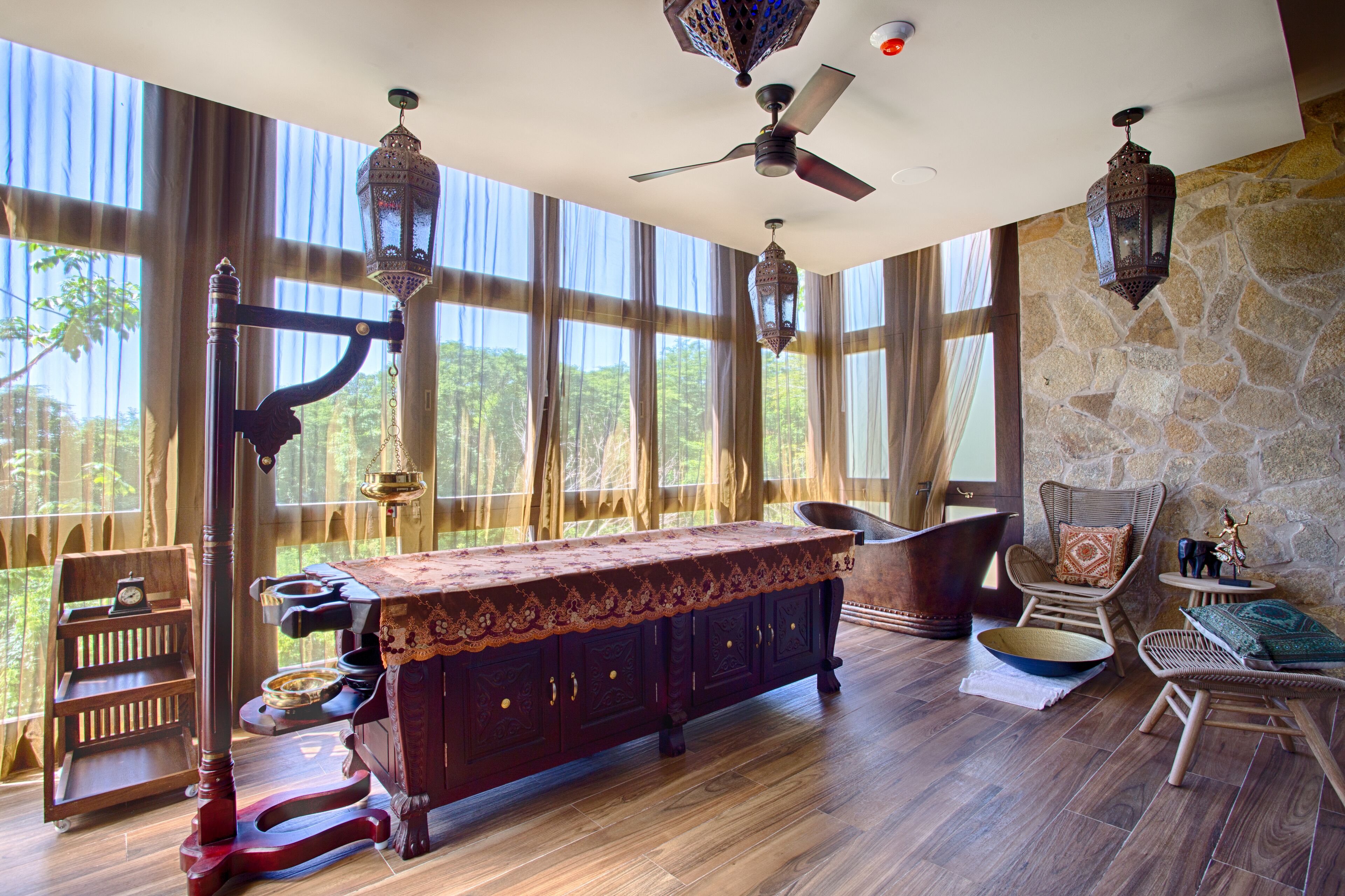 A spacious room with a large wooden table, a ceiling fan, and a stone wall.