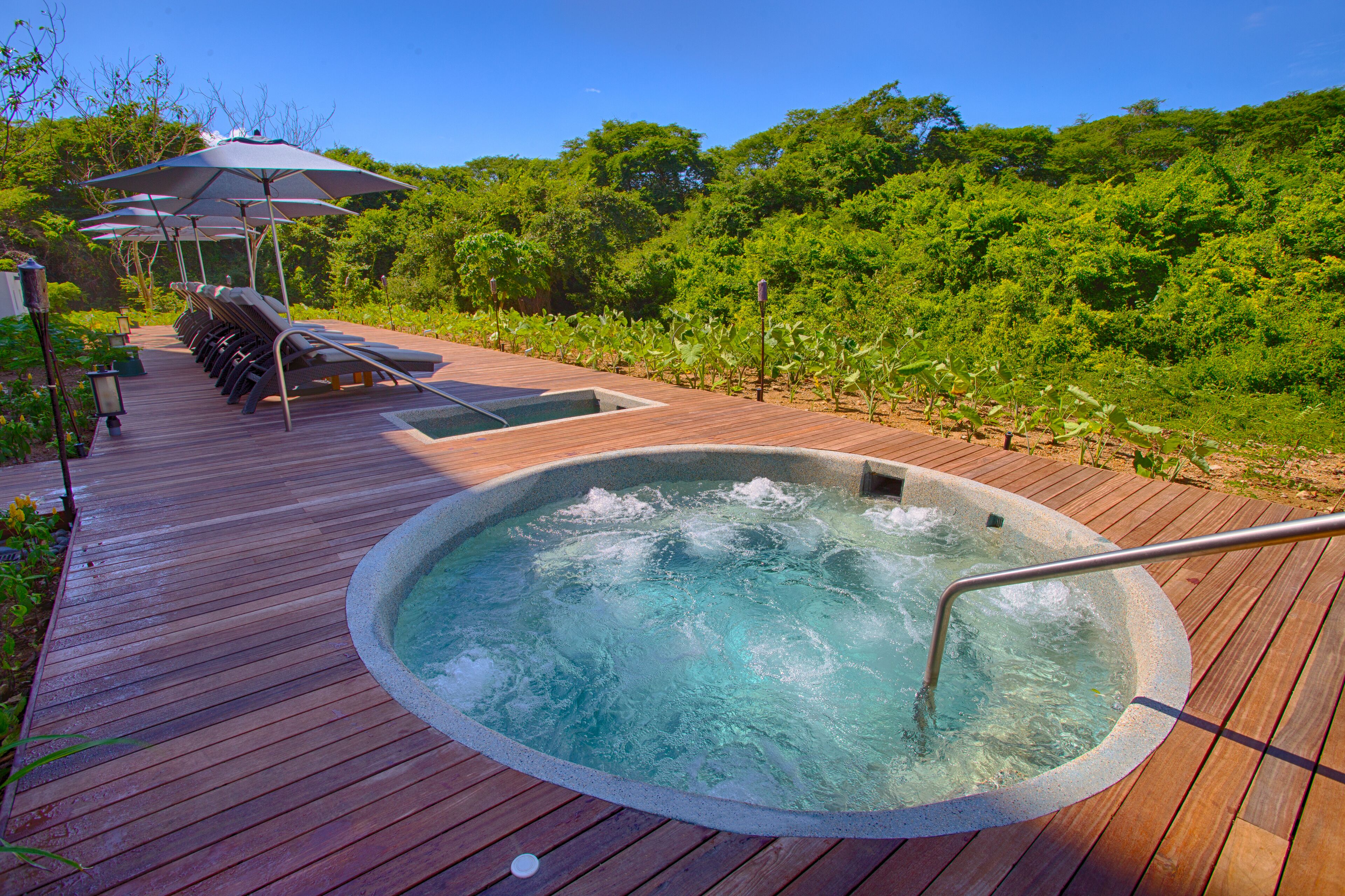 Una terraza de madera con jacuzzi, sillas de descanso y sombrillas.