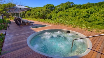 Una terraza de madera con jacuzzi, sillas de descanso y sombrillas.
