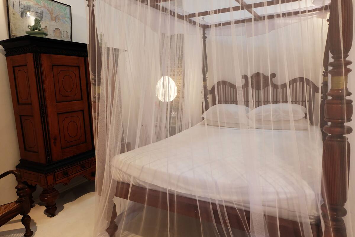A four-poster bed with a canopy, a wooden cabinet, and a framed picture on the wall.