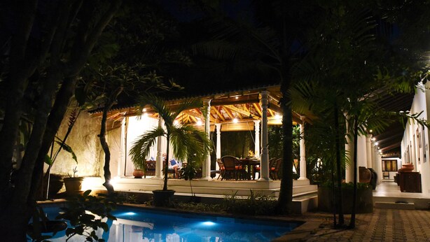 A poolside area with a covered seating area, palm trees, and a well-lit patio. - Orchard House (Galle)