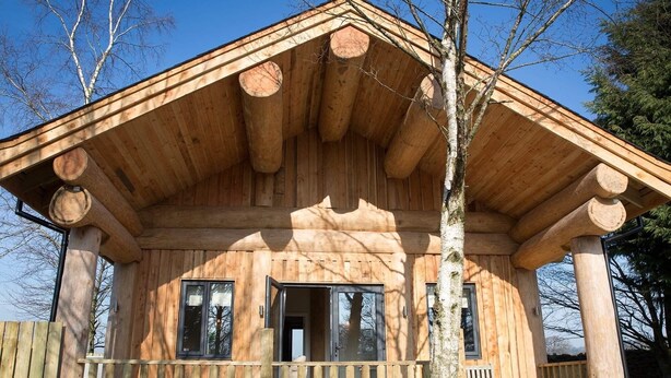 A wooden cabin with a porch, large windows, and a chimney. - Braisty Woods - Knotty & Nice (Harrogate)