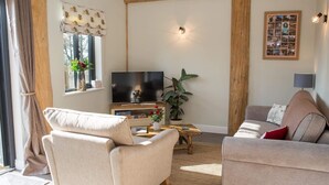 A cozy living room with a flat-screen TV, two sofas, a coffee table, and a window with curtains. - Braisty Woods - Knotty & Nice (Harrogate)