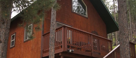 A wooden cabin with a balcony, surrounded by trees.