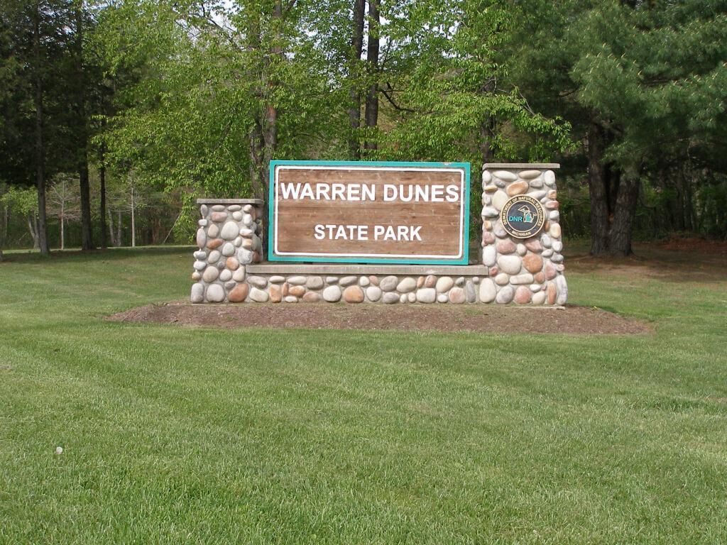 Un panneau indiquant l’entrée du parc d’État de Warren Dunes, avec un mur en pierre et un logo.