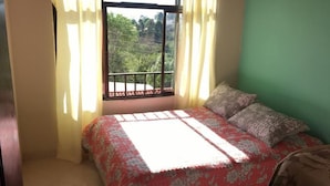 Une chambre à coucher avec un lit, une fenêtre avec des rideaux et une vue sur la verdure.