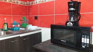 Une cuisine équipée d’un micro-ondes noir, d’une machine à café et de divers ustensiles de cuisine disposés sur le plan de travail.
