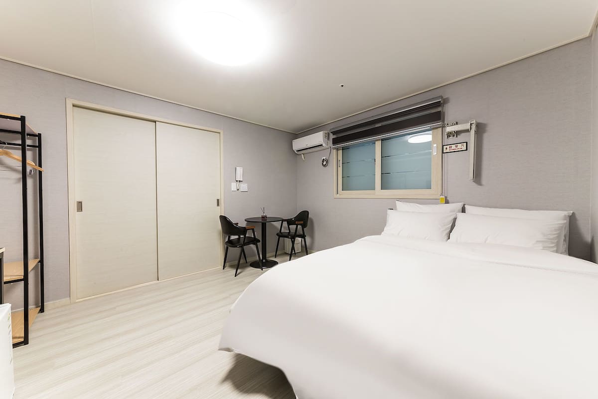 Habitación de hotel con cama, escritorio, sillas, ventana y aire acondicionado.
