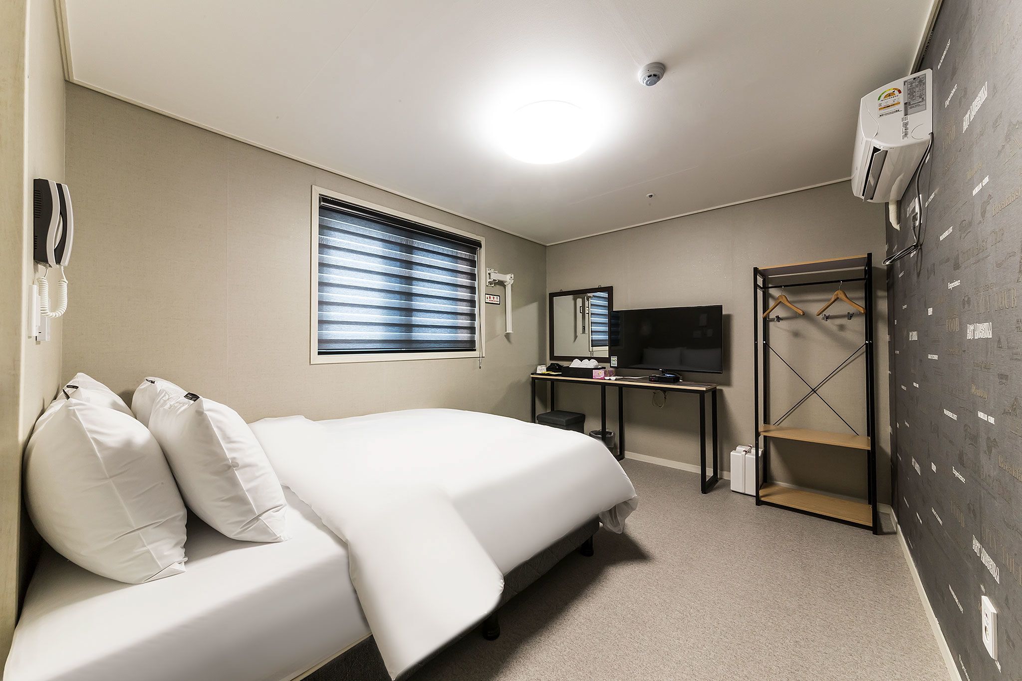 A hotel room with a bed, a desk, a TV, a wardrobe, and a window with blinds.
