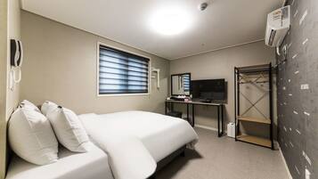 A hotel room with a bed, a desk, a TV, a wardrobe, and a window with blinds.