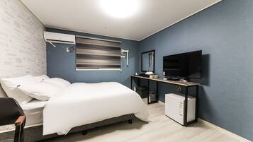A modern bedroom with a bed, a desk, a television, and an air conditioning unit.