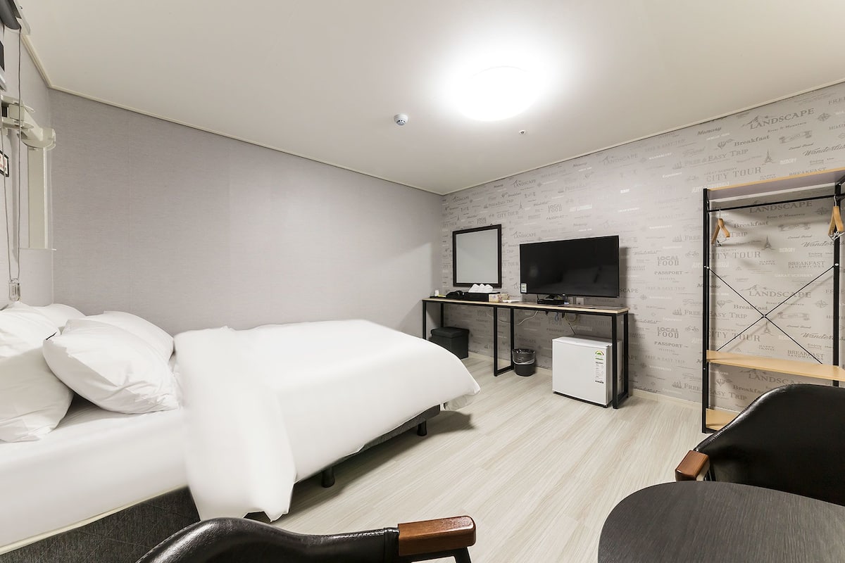 Una habitación de hotel moderna con cama, escritorio, silla, televisor y armario.