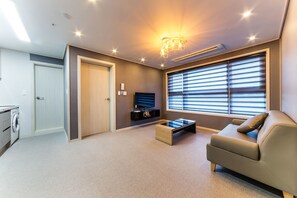 Un salon moderne avec un canapé, une table basse, un téléviseur et une fenêtre équipée de stores.