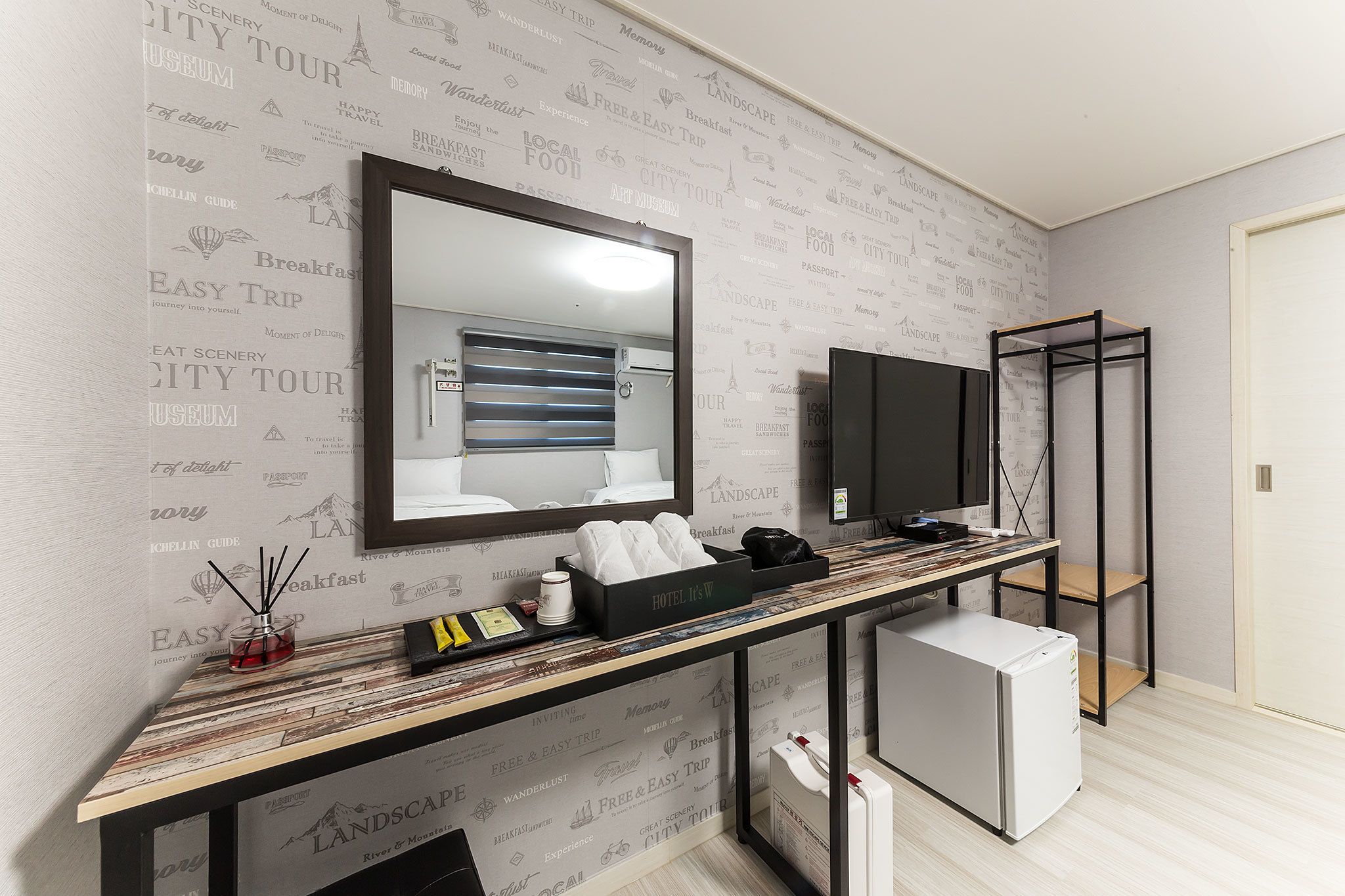 A hotel room with a large mirror, a television, a minibar, and a small refrigerator.