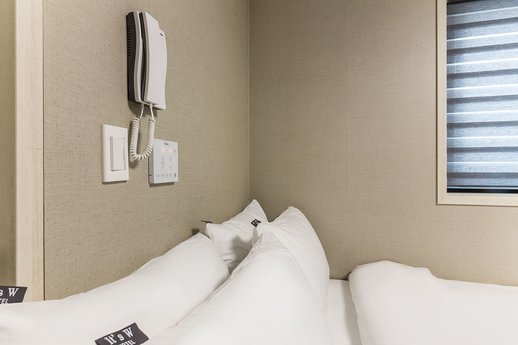 Una habitación de hotel con una cama, un teléfono y una ventana con persianas.