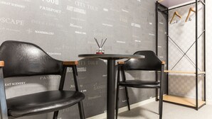 Une pièce comprenant deux fauteuils en cuir noir, une petite table ronde et un porte-manteau suspendu.