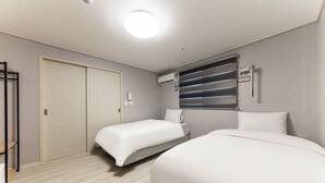 Une chambre d’hôtel avec deux lits, une armoire, un appareil de climatisation et une fenêtre avec des stores.