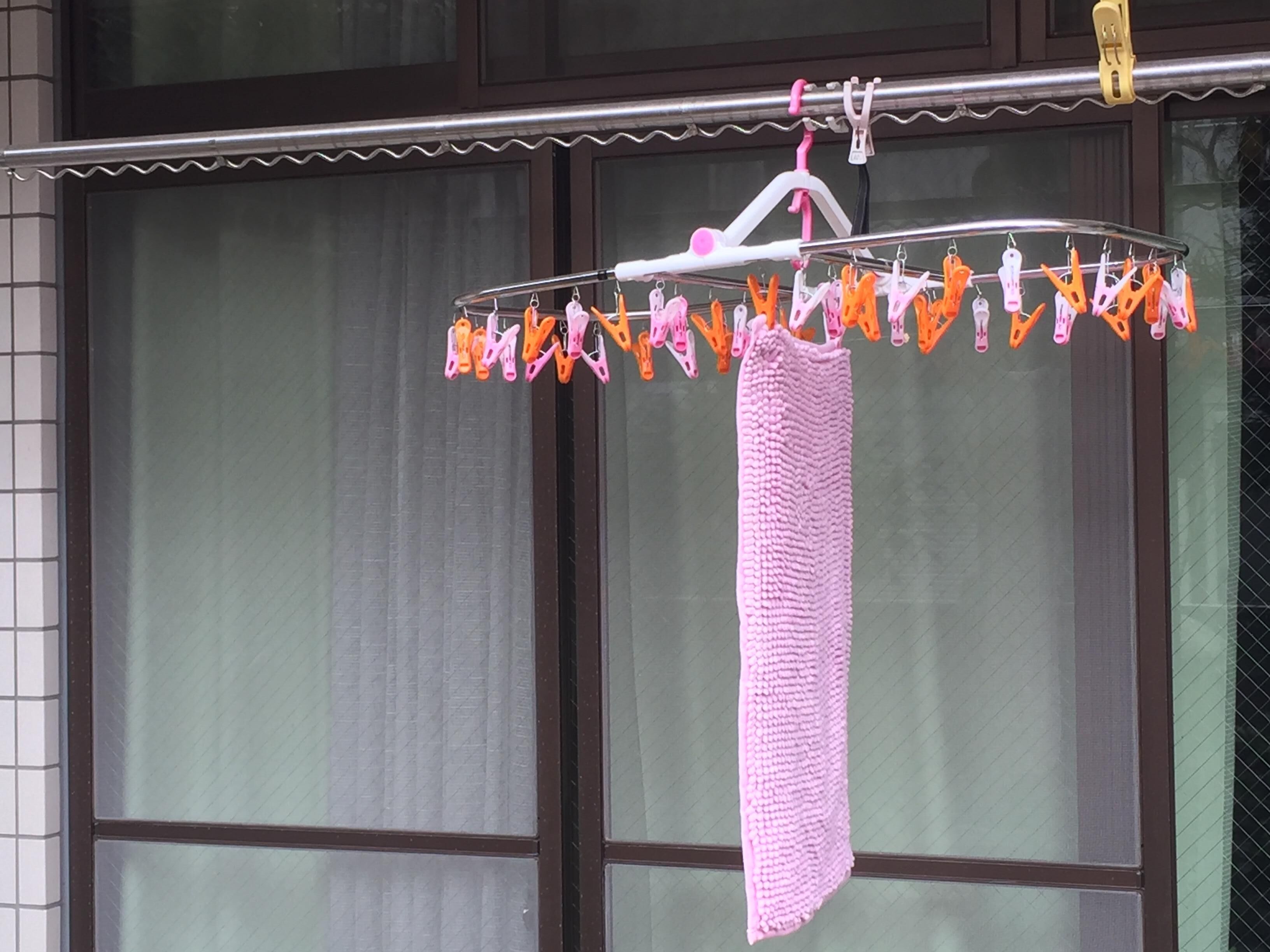 A drying rack with multiple clothespins, a pink towel, and a window with blinds in the background.